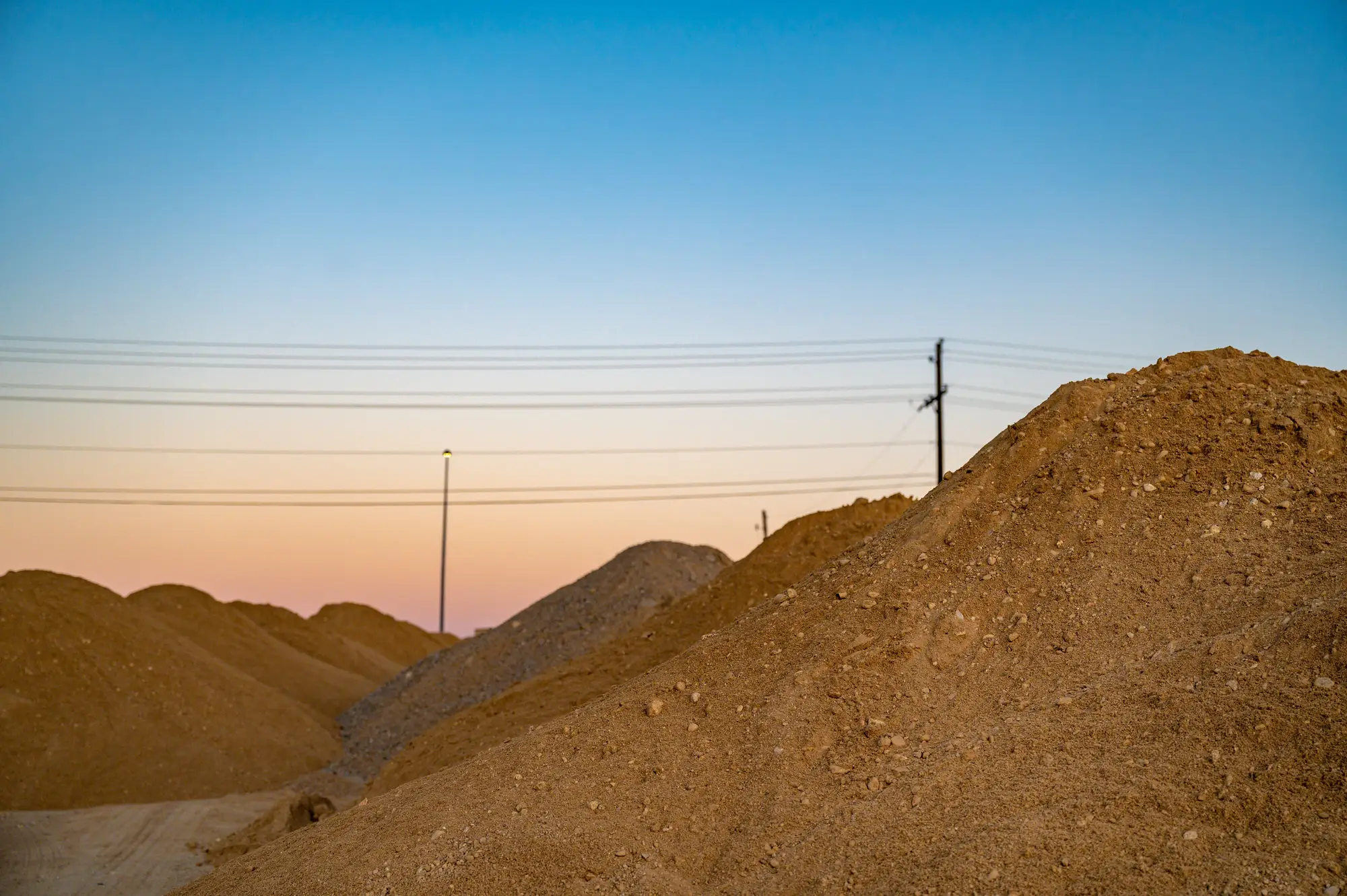 Mounds of excavated soil on a site at dusk, with power lines behind